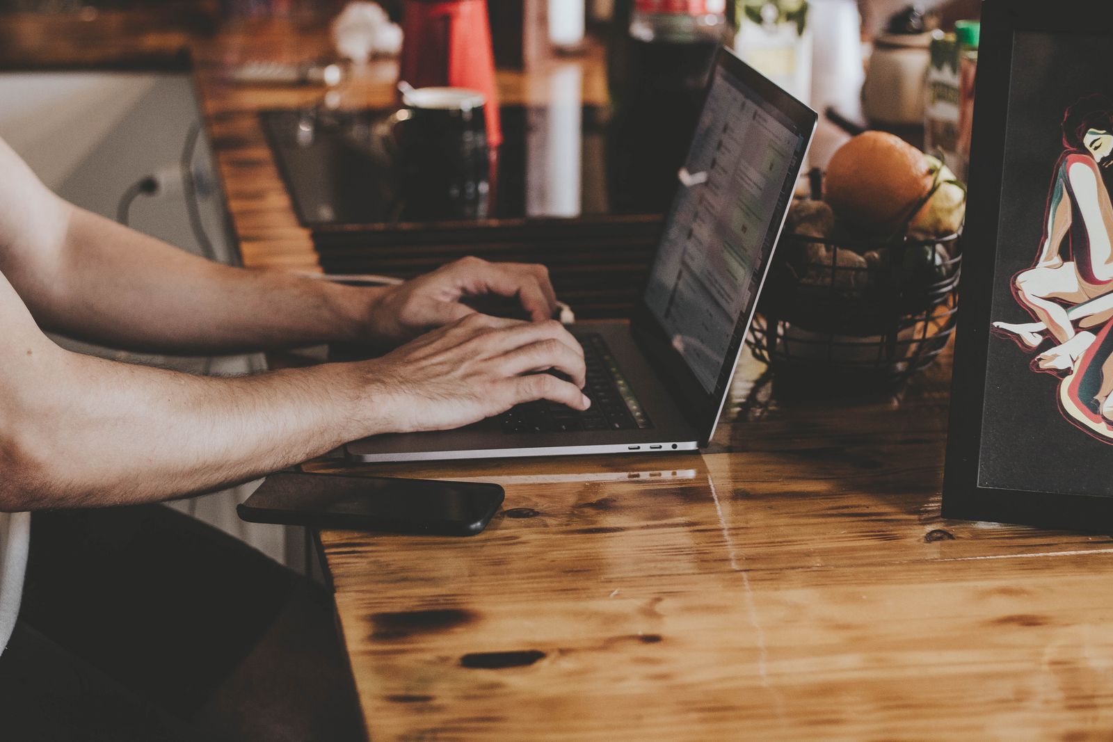 Hands on a laptop at a warm wooden bar — the twenty minutes a week merchants actually spend inside OmniPost.